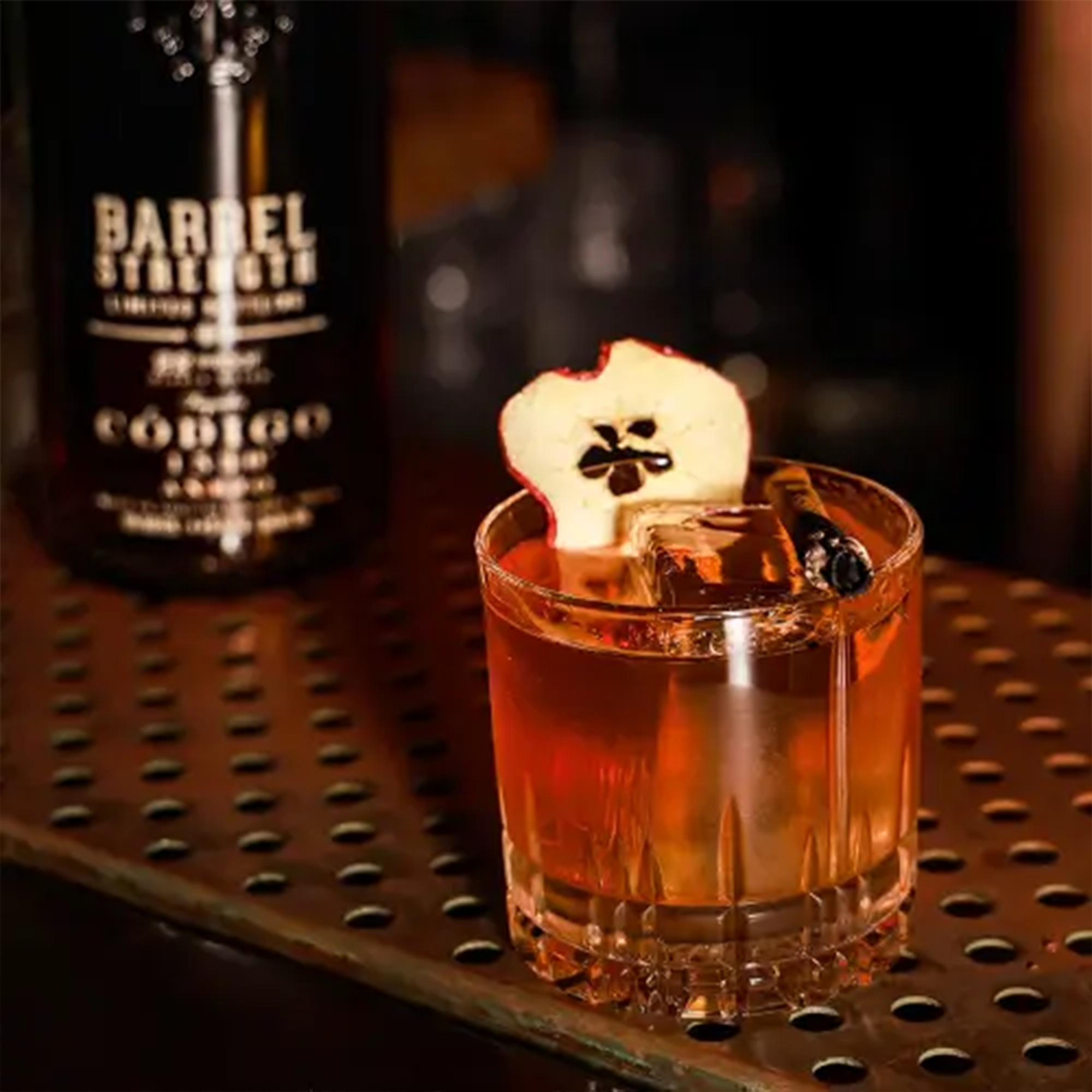 Cocktail with Código 1530 Añejo tequila garnished with a dried apple slice on a bar top.