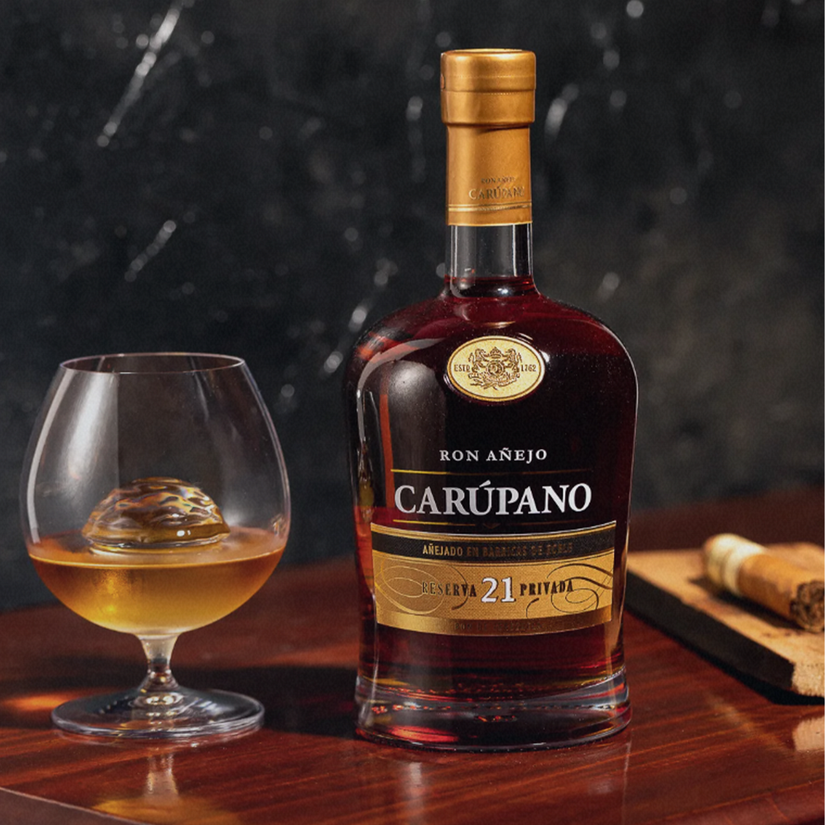 Ron Carupano Riserva Privada 21 Year Anejo Rum bottle next to a glass of golden rum on a wooden table.