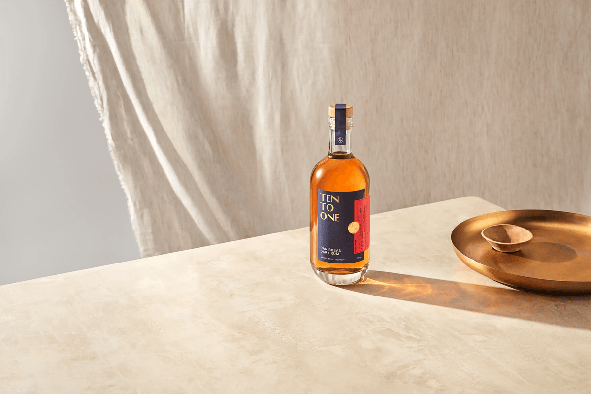 Ten To One Caribbean Dark Rum bottle on a light surface with a metallic plate, showcasing its rich amber color.