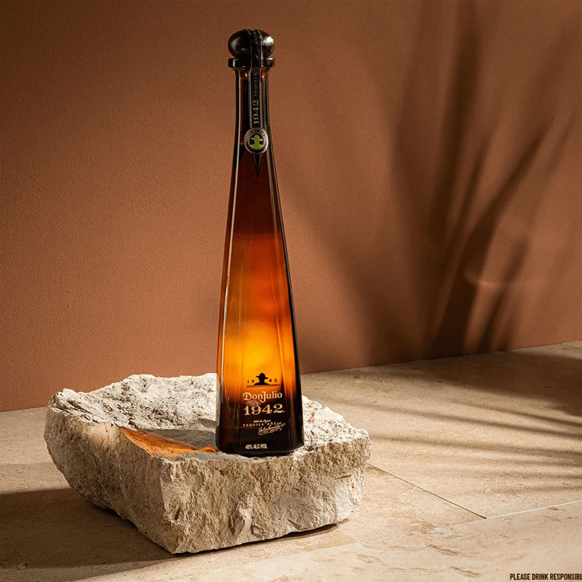 Don Julio Añejo 1942 tequila bottle displayed on a stone base, showcasing its elegant design and rich amber color.