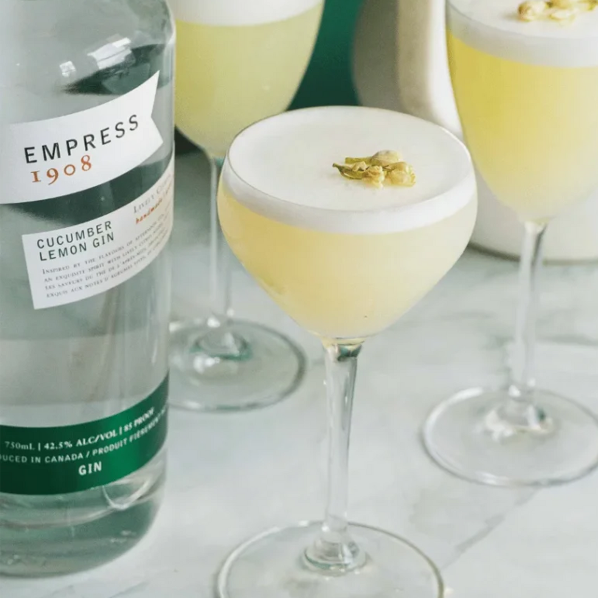 Empress 1908 Cucumber Lemon Gin bottle with cocktails garnished, showcasing vibrant yellow colors and fresh ingredients.