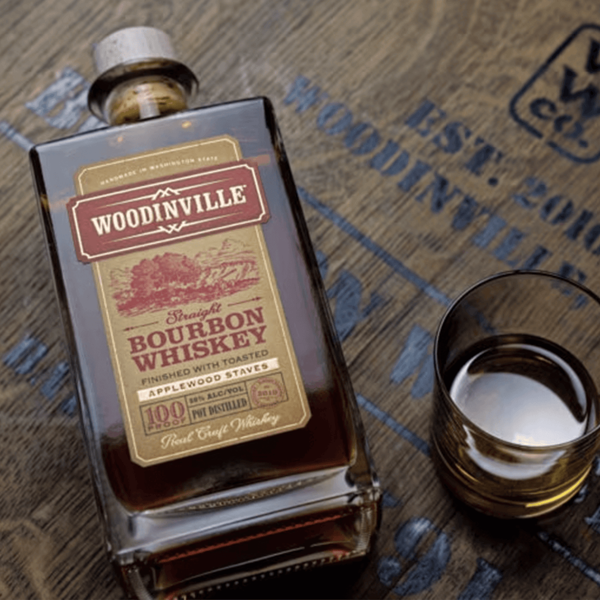 Woodinville Applewood Staves Straight Bourbon Whiskey bottle and glass on rustic wood surface.