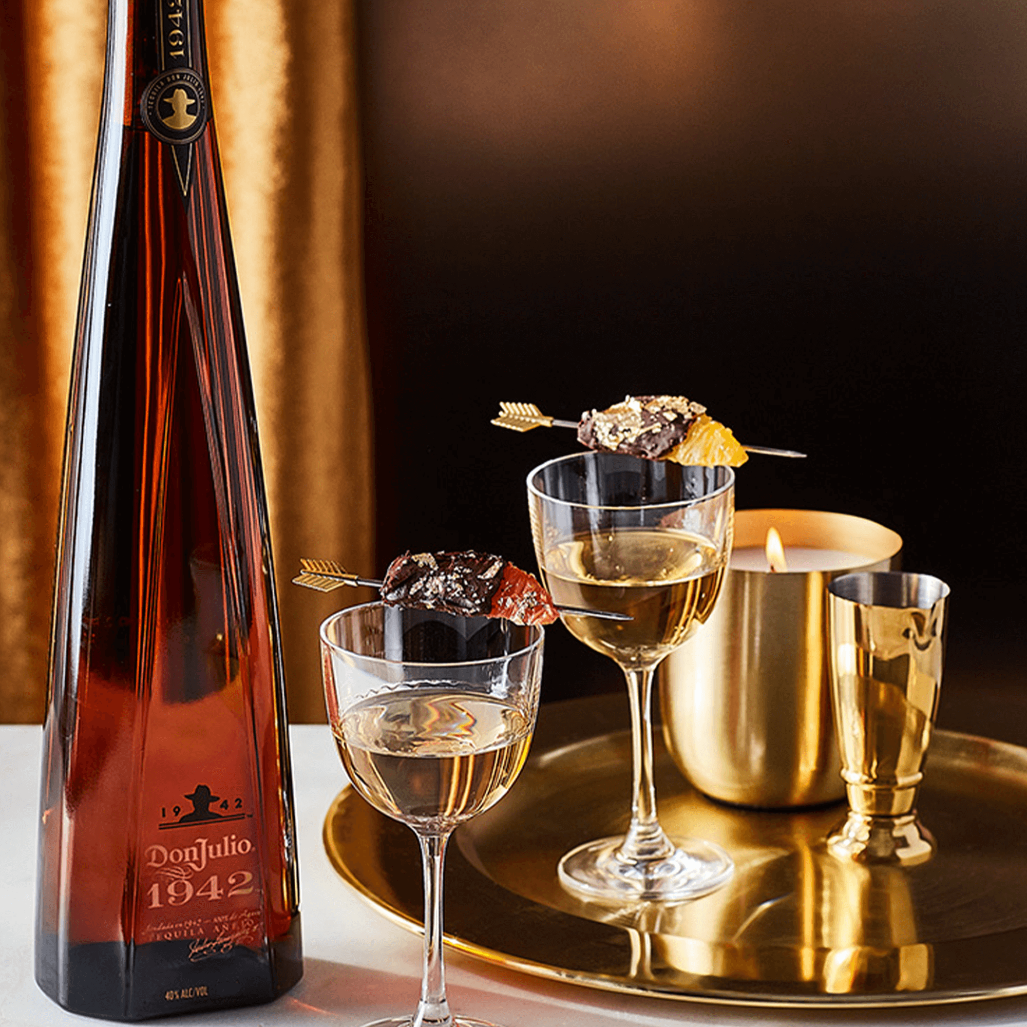 Bottle of Don Julio 1942 tequila with elegant cocktails and a candle on a stylish table setting.