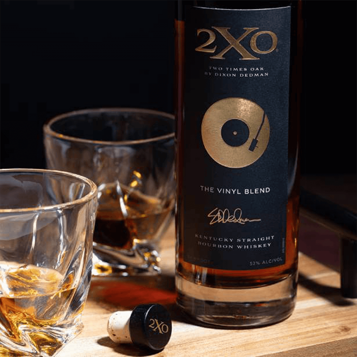 2XO The Vinyl Blend bourbon whiskey bottle with glasses of whiskey on a wooden surface, celebrating music and craftsmanship.