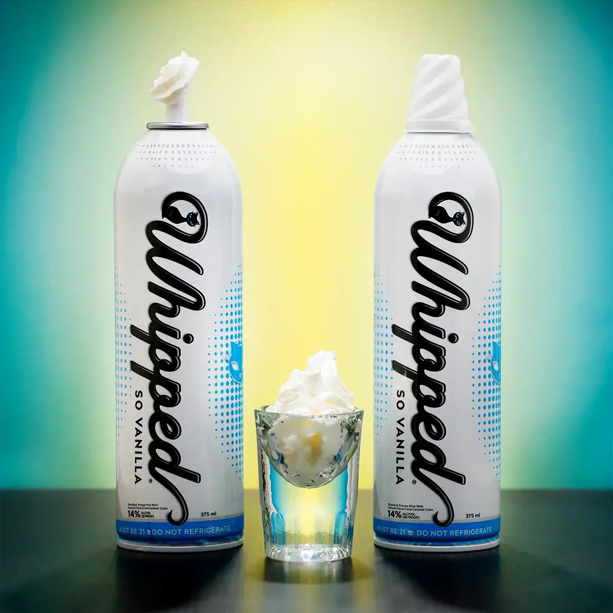 Two cans of Lick the Whip So Vanilla alcohol-infused whipped cream with a shot glass of whipped cream.