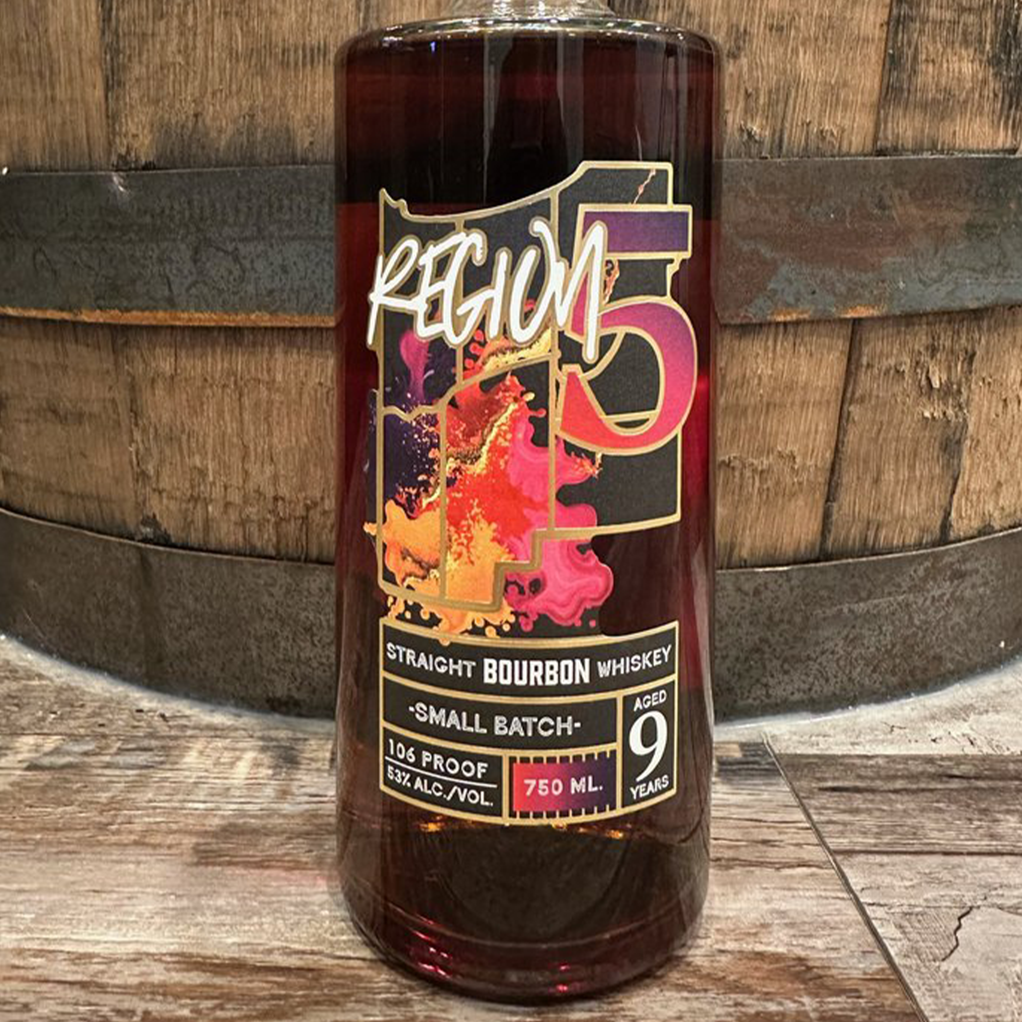 Bottle of Region 5 Small Batch 9 Year Bourbon whiskey with colorful label and aged barrel background.