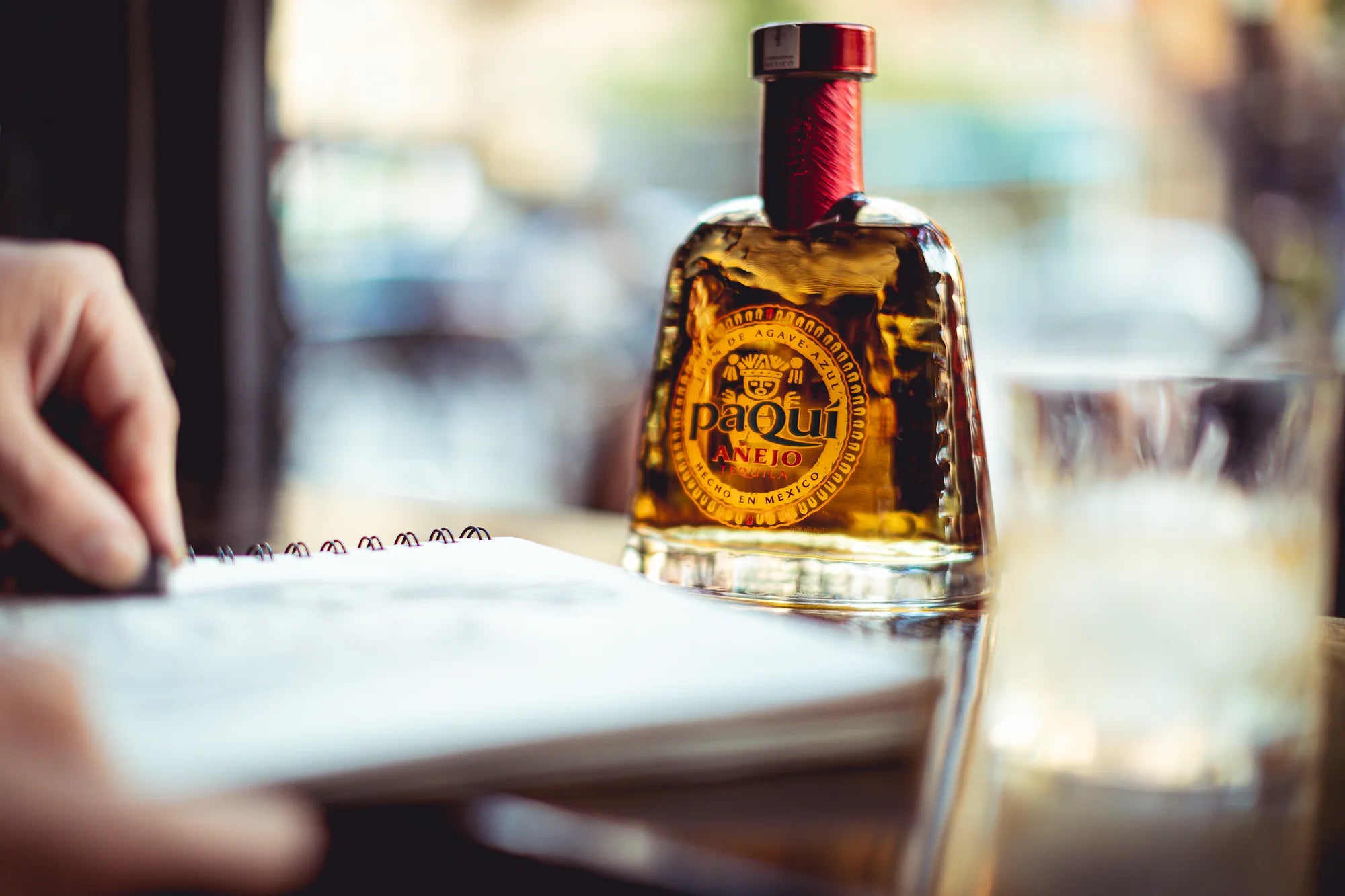 PaQuí Añejo Tequila bottle on a table beside a sketchbook and a glass, showcasing its artisanal craftsmanship and rich flavor.