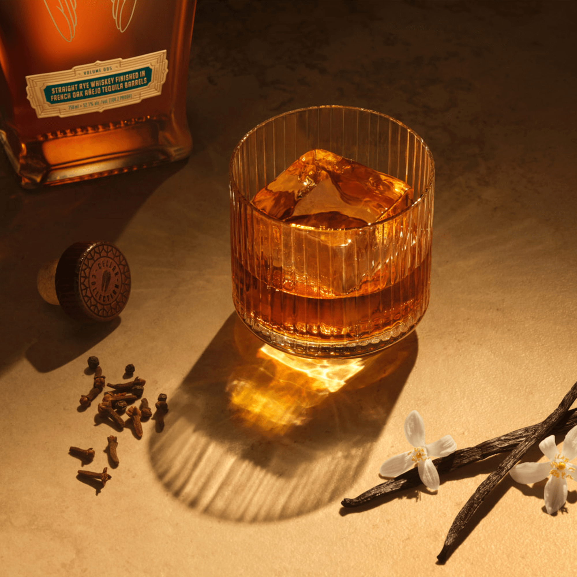 Glass of Angel's Envy Straight Rye Whiskey with ice, vanilla, and aromatic spices on a textured surface.