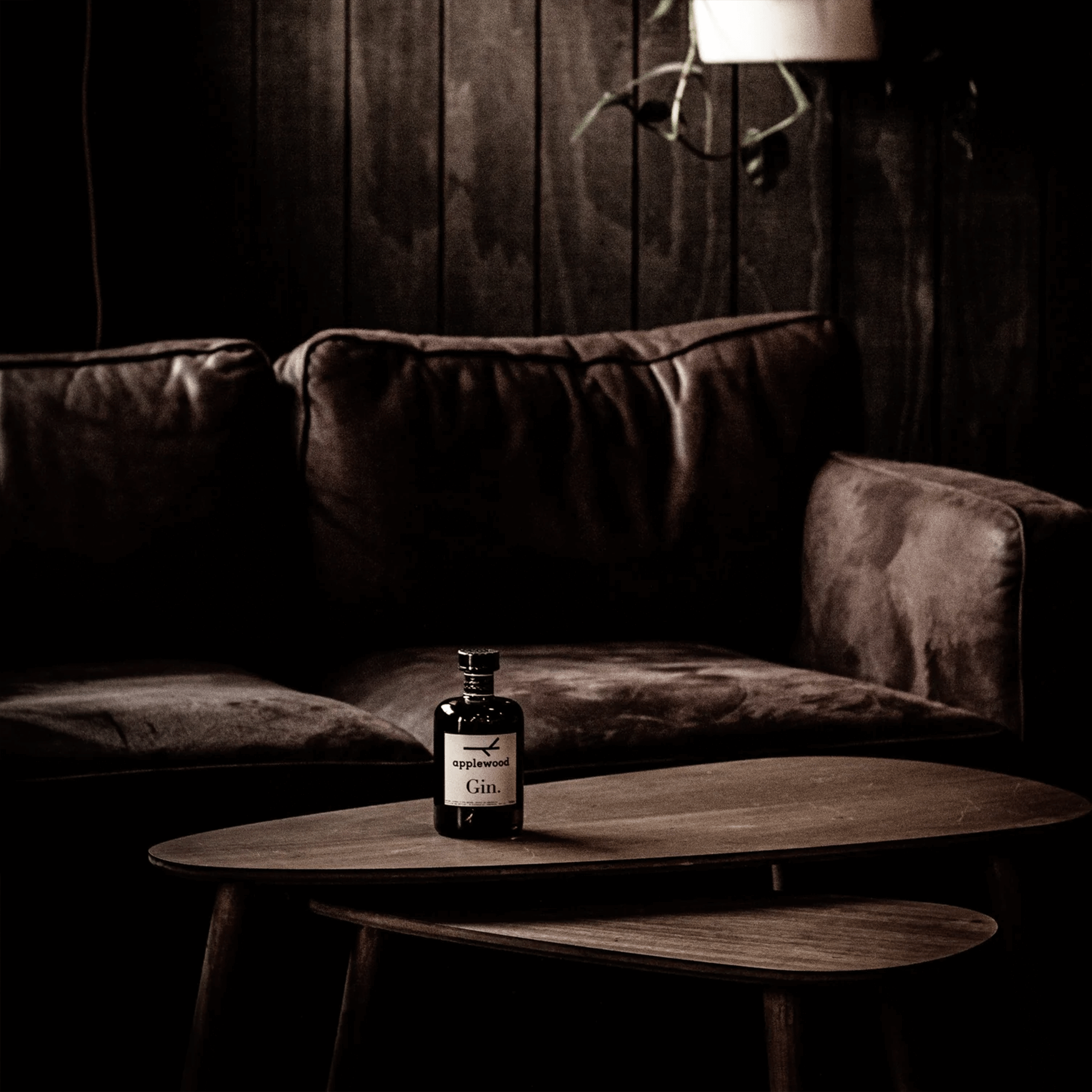 Bottle of Applewood Australian Gin on a wooden table in a cozy, dark living room setting.