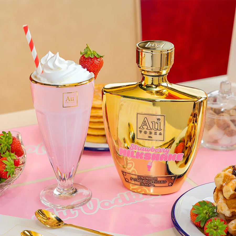 Au Vodka Strawberry Milkshake Liqueur bottle next to a strawberry milkshake, strawberries, and pancakes.