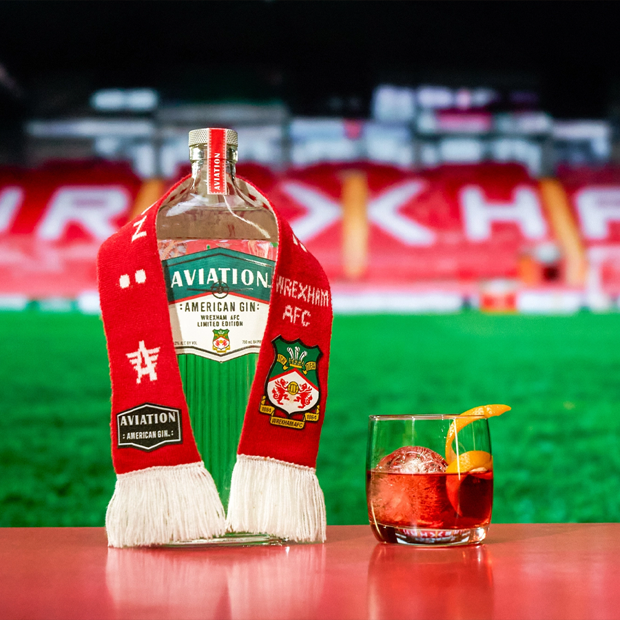 Aviation Gin bottle with Wrexham AFC scarf and cocktail on a table, celebrating the team's spirit.