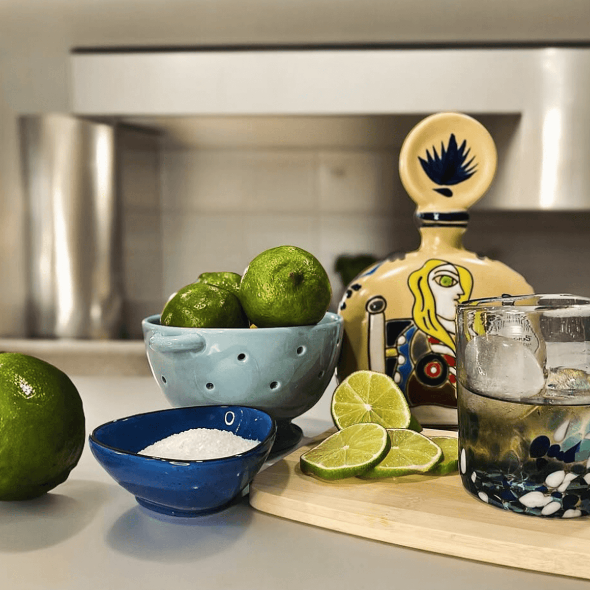 Azulejos Añejo Yellow Tequila bottle with limes, salt, and a cocktail glass on a wooden board.