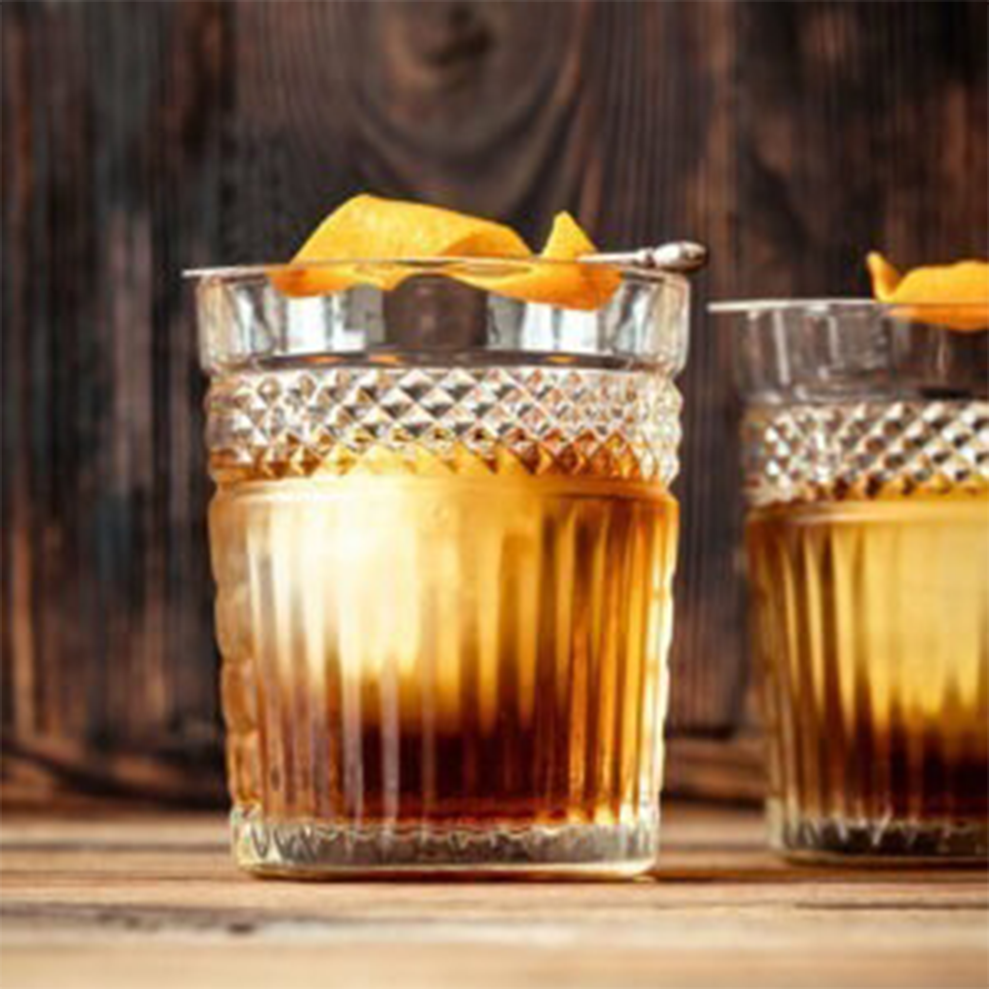 Two glasses of Bird Dog Peanut Butter Whiskey cocktails garnished with orange, set on a rustic wooden background.