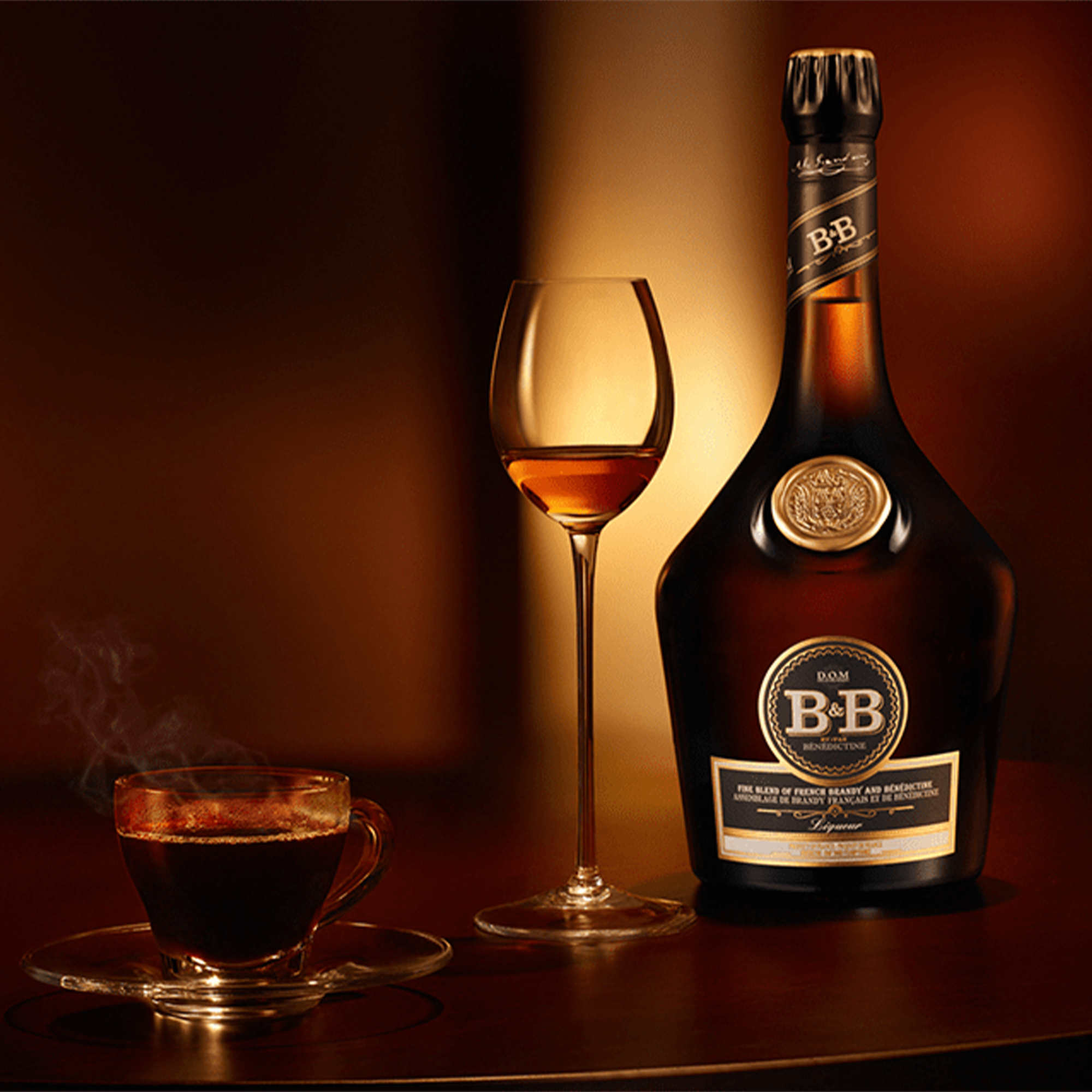B&B Benedictine Brandy Liqueur bottle beside a glass and a steaming cup on a wooden surface.