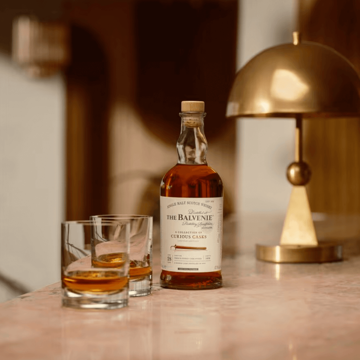 Bottle of Balvenie 18 Year French Pineau Cask Scotch with two glasses on a stylish countertop.
