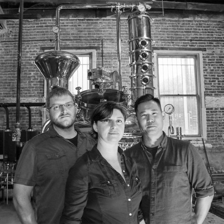 Barber Lee White Rum distillers standing in front of distillation equipment in a vintage distillery setting.