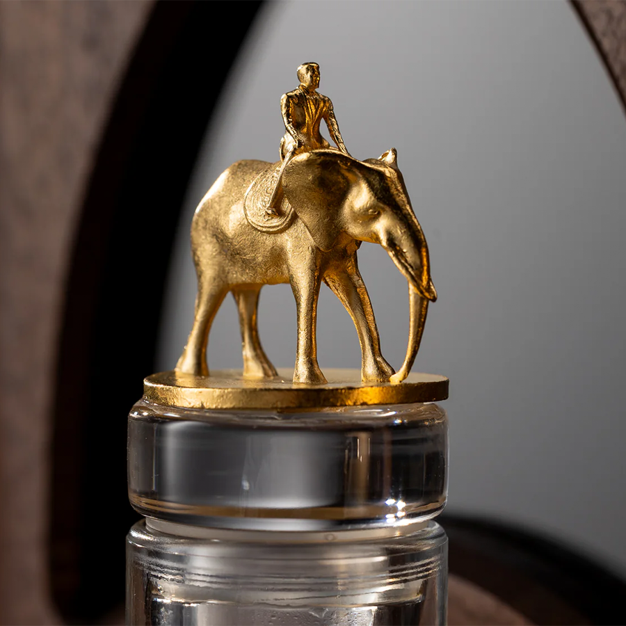Gold elephant figurine with a rider atop, resting on a clear glass bottle.