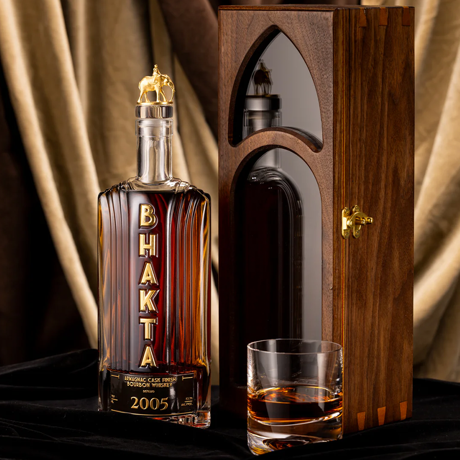 Bhakta 2005 Bourbon Whiskey in elegant glass bottle with wooden case and glass of whiskey.