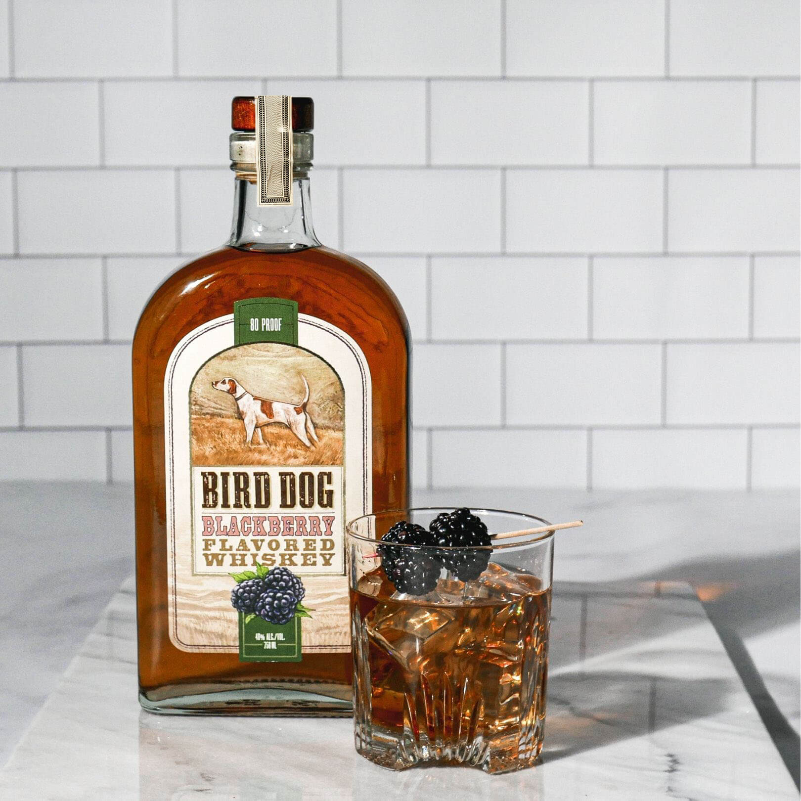 Bird Dog Blackberry Whiskey bottle next to a glass of whiskey with blackberries, showcasing its distinctive flavor.