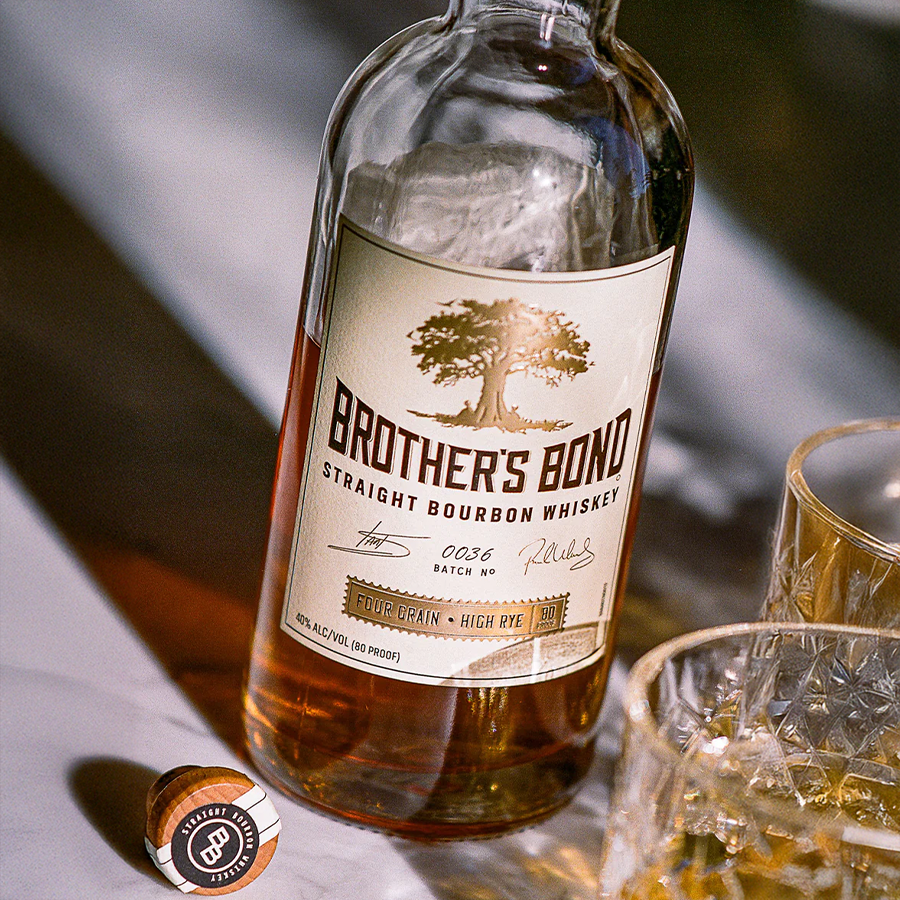 Brother's Bond Straight Bourbon Whiskey bottle with glass and cap on marble surface.