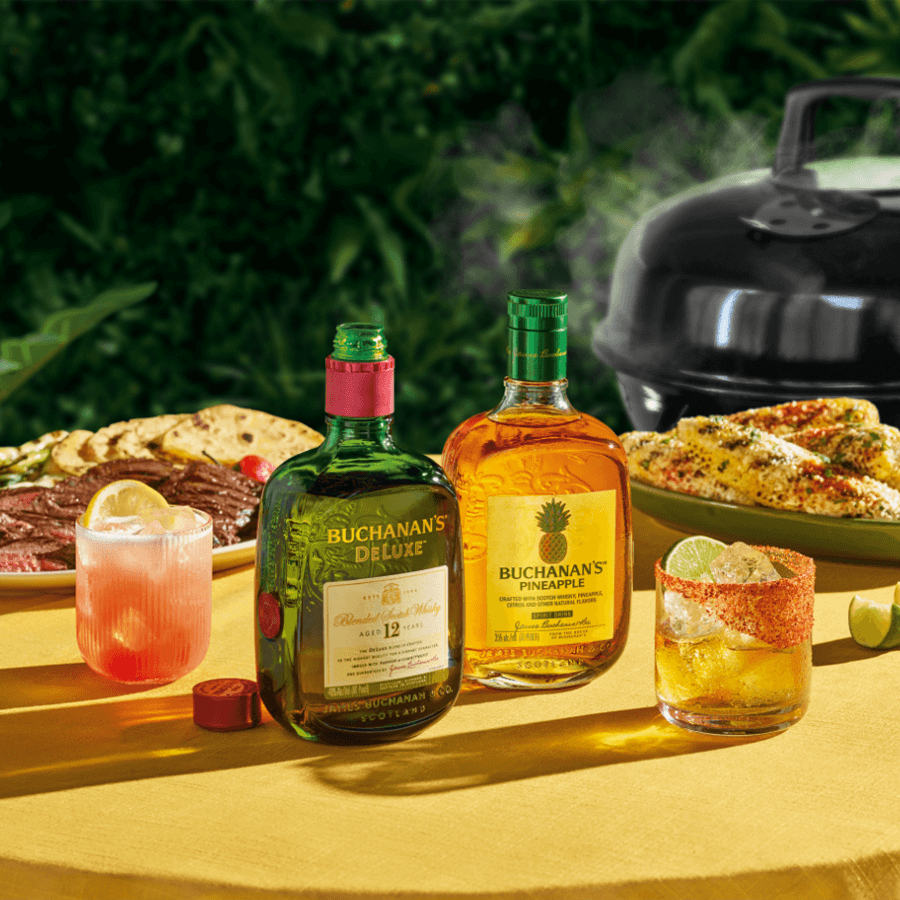 Buchanan's Pineapple Scotch and Deluxe whisky on a table with grilled food and cocktails, perfect for summer gatherings.