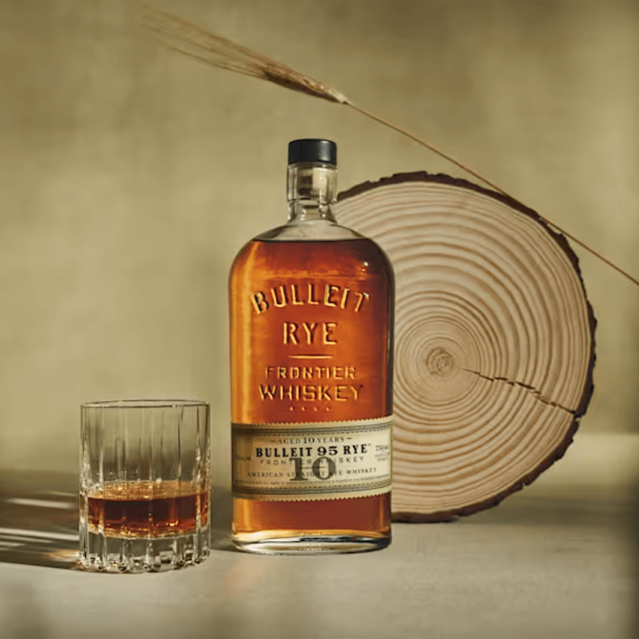 Bulleit 95 Rye 10 Year Frontier Whiskey bottle with glass on wooden background, showcasing its rich amber color.