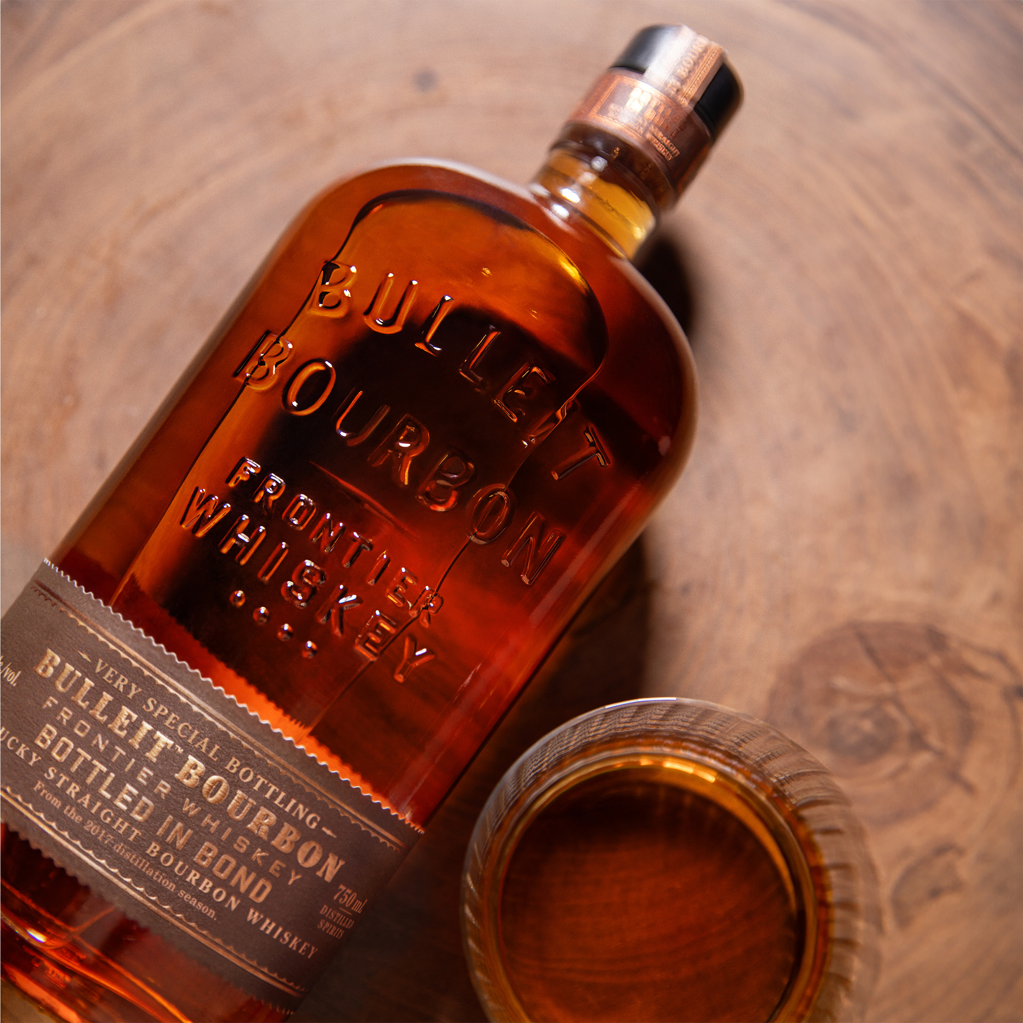 Bulleit Bottled in Bond Kentucky Straight Bourbon bottle with a glass of whiskey on a wooden surface.