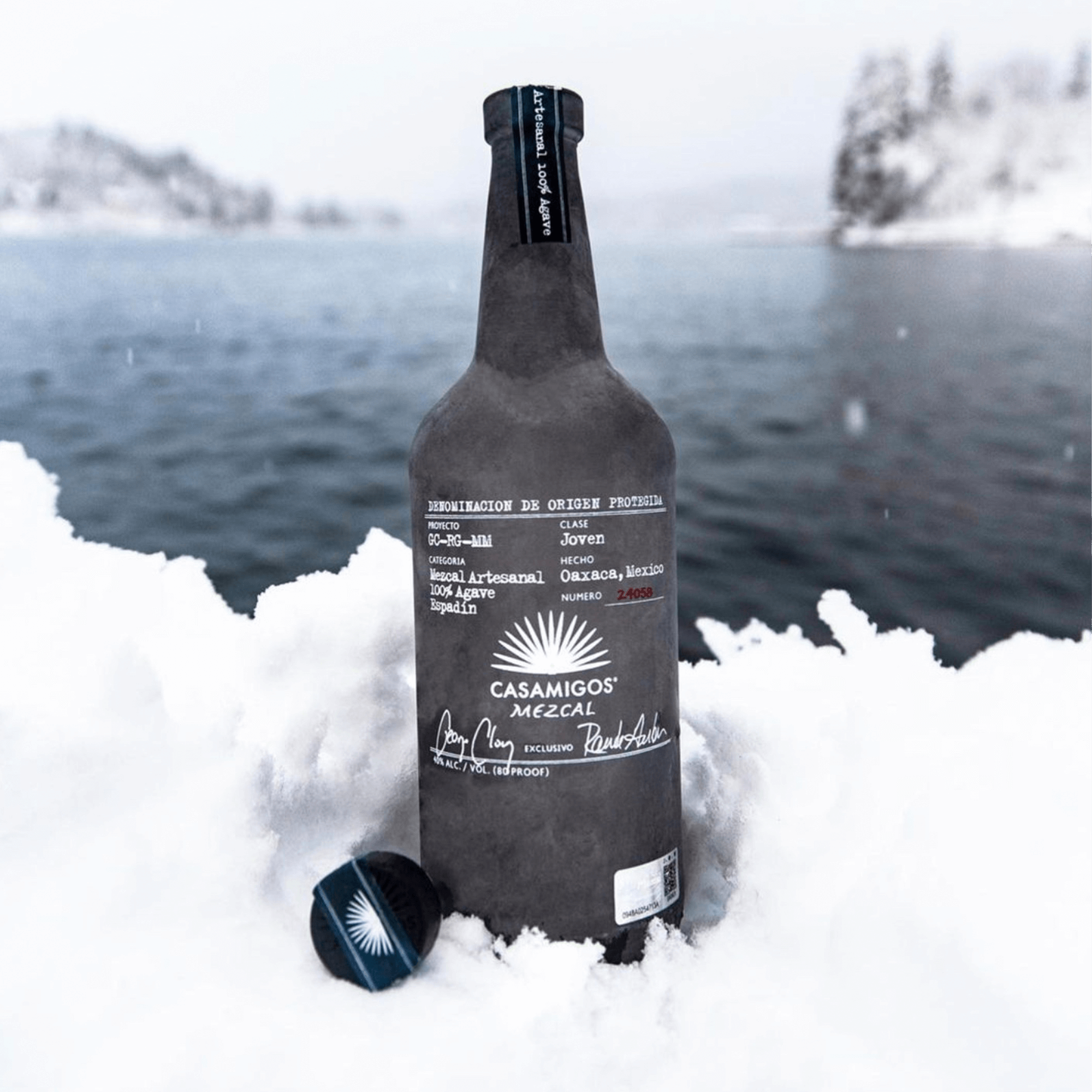 Casamigos Mezcal 1L bottle in snow by a lake, showcasing its elegant design and brand label.
