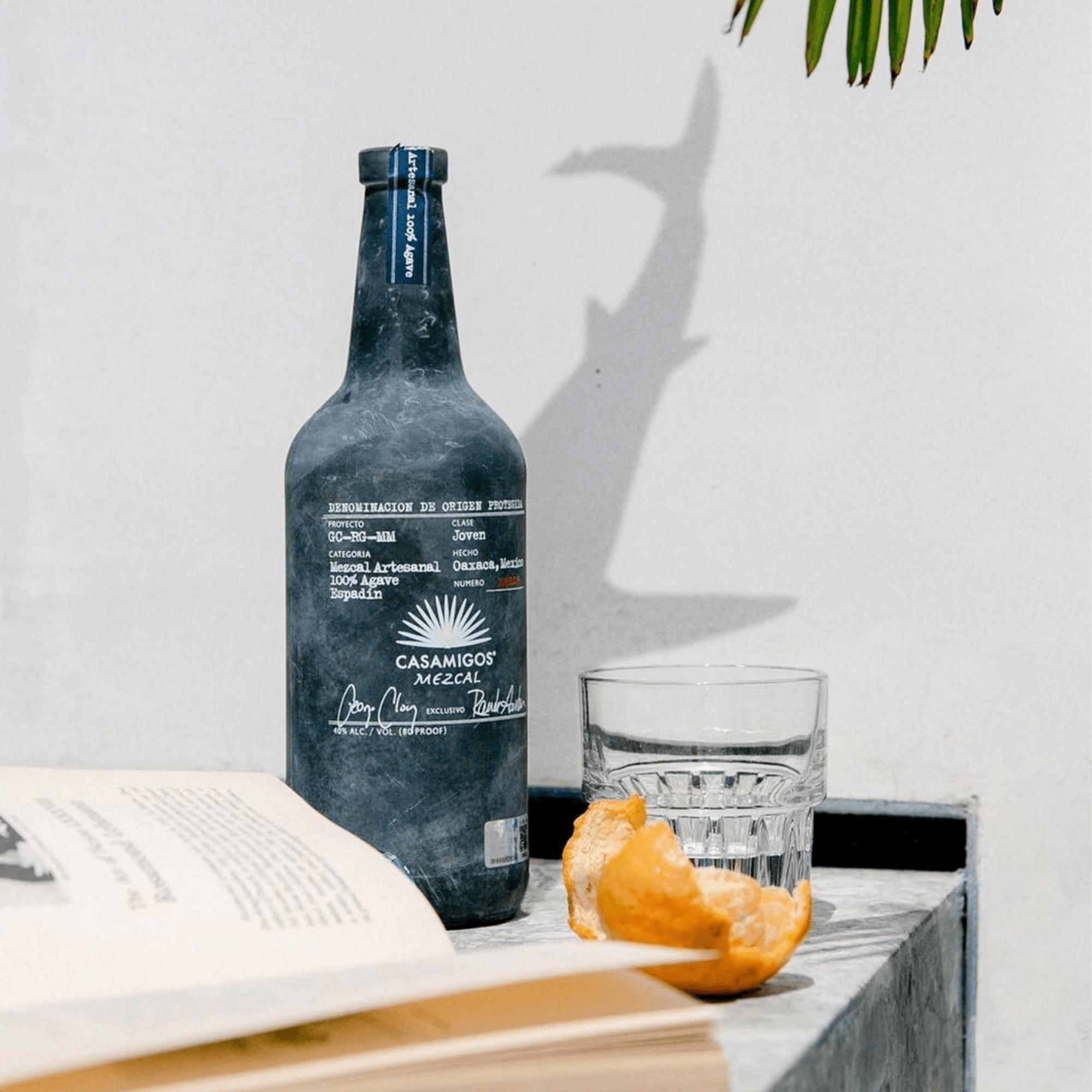 Casamigos Mezcal 1L bottle on marble table with glass, book, and orange peel, showcasing its elegant design.