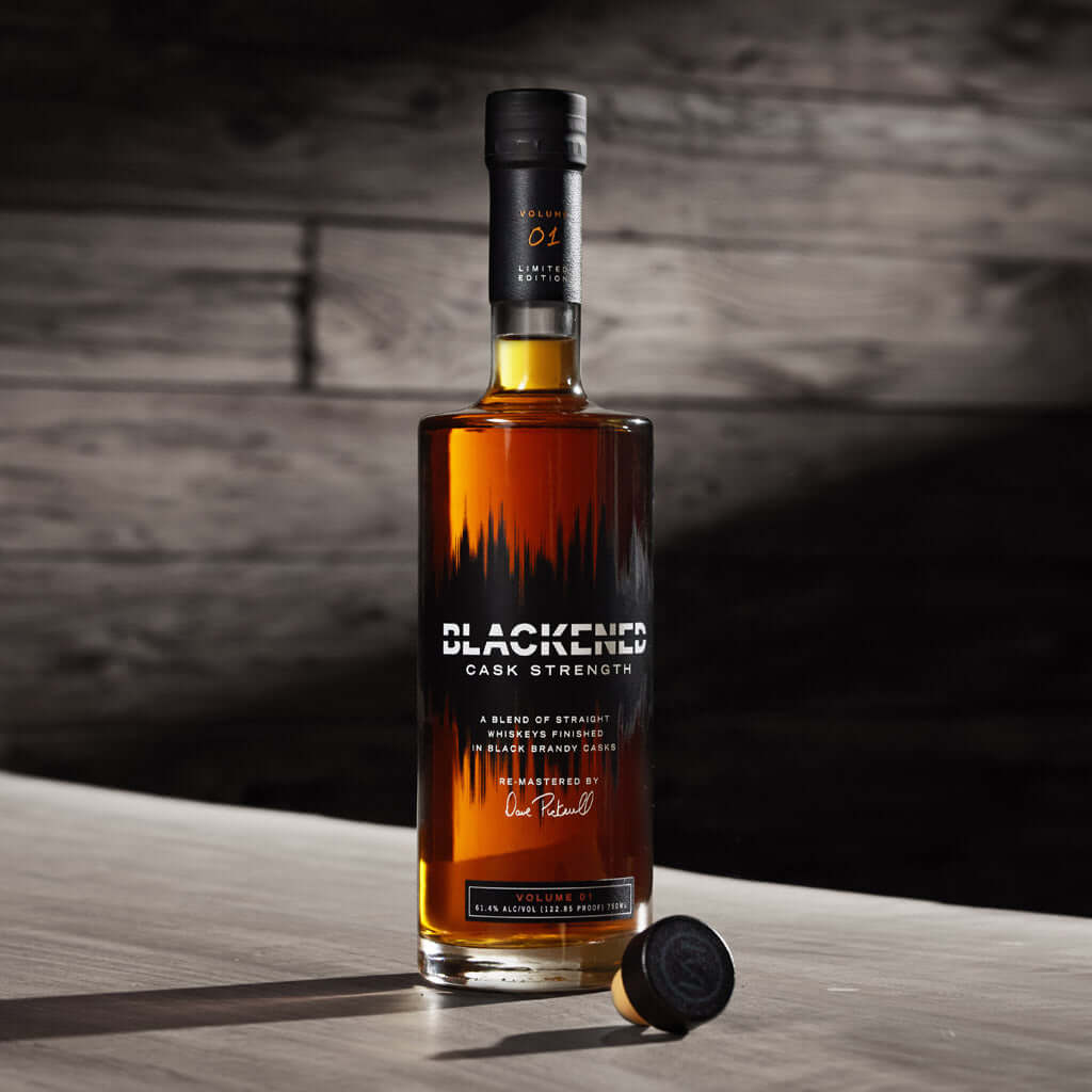 Blackened Volume 1 Cask Strength Blended Whiskey bottle on a wooden table, showcasing its rich amber color and unique label.