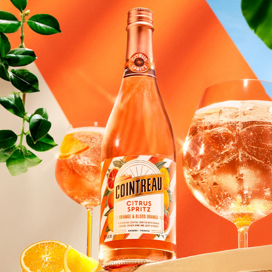 Cointreau Citrus Spritz Orange & Blood Orange bottle with two glasses of citrus spritz cocktails and fresh orange slices.