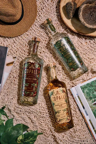 Three Copalli rum bottles displayed on a woven surface, showcasing unique designs of Cacao and Barrel Rested varieties.