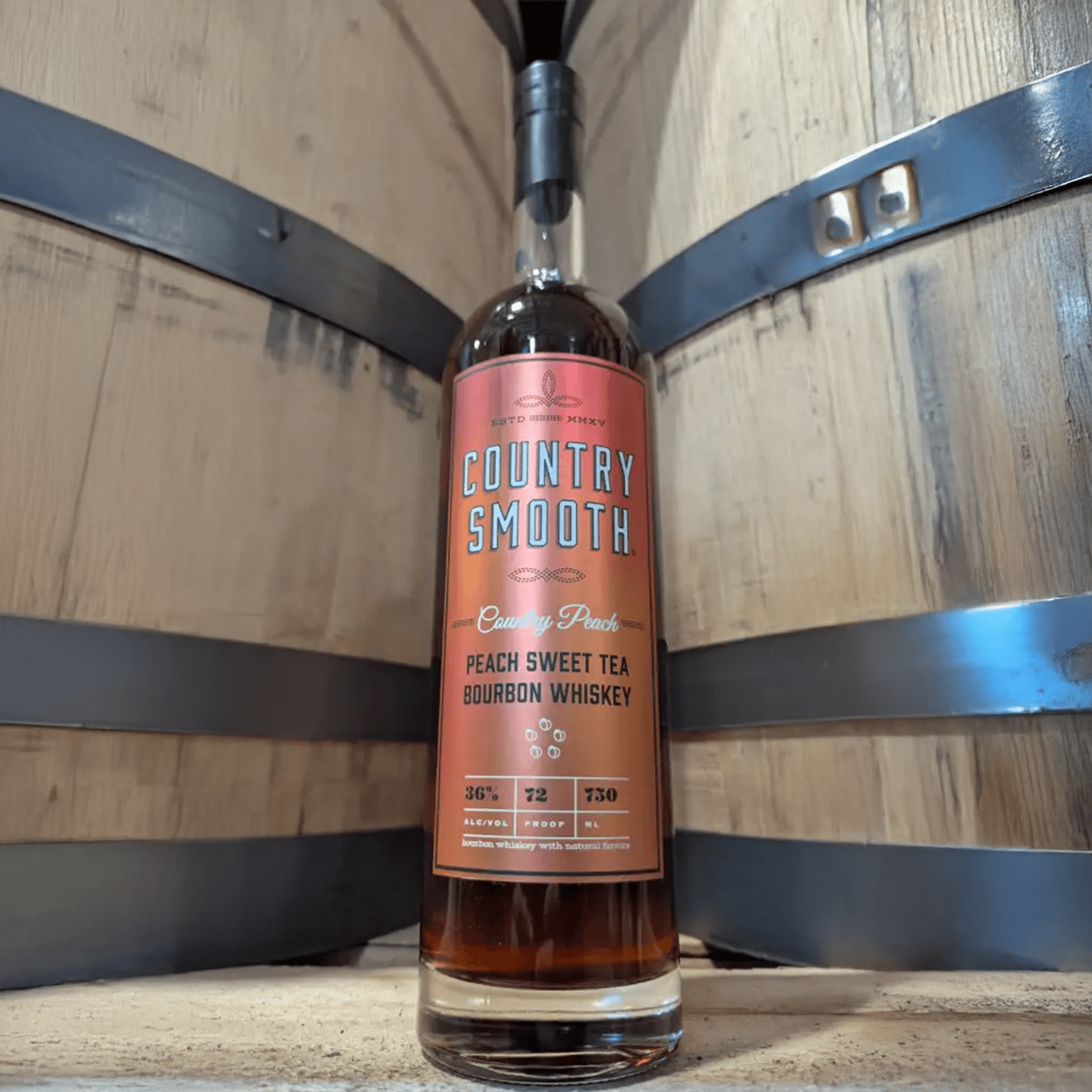 Country Smooth Peach Sweet Tea Bourbon Whiskey bottle against a wooden barrel backdrop.
