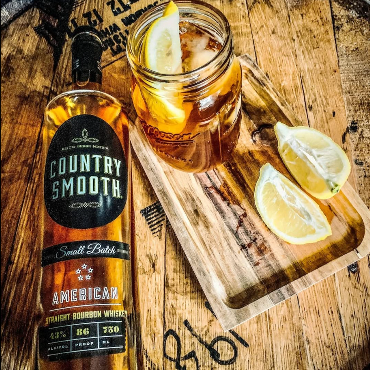 Country Smooth Small Batch Bourbon whiskey bottle beside a refreshing drink with lemon slices on a wooden surface.