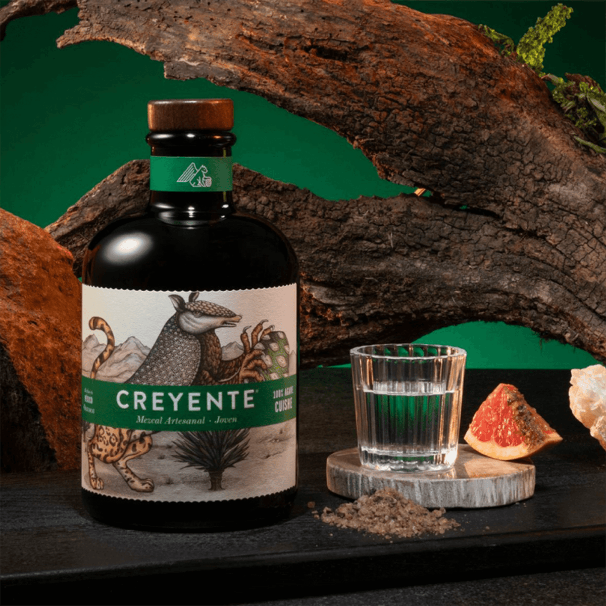 Creyente Cuishe Mezcal bottle with shot glass, featuring Cuishe agaves and artisan label, on rustic backdrop.