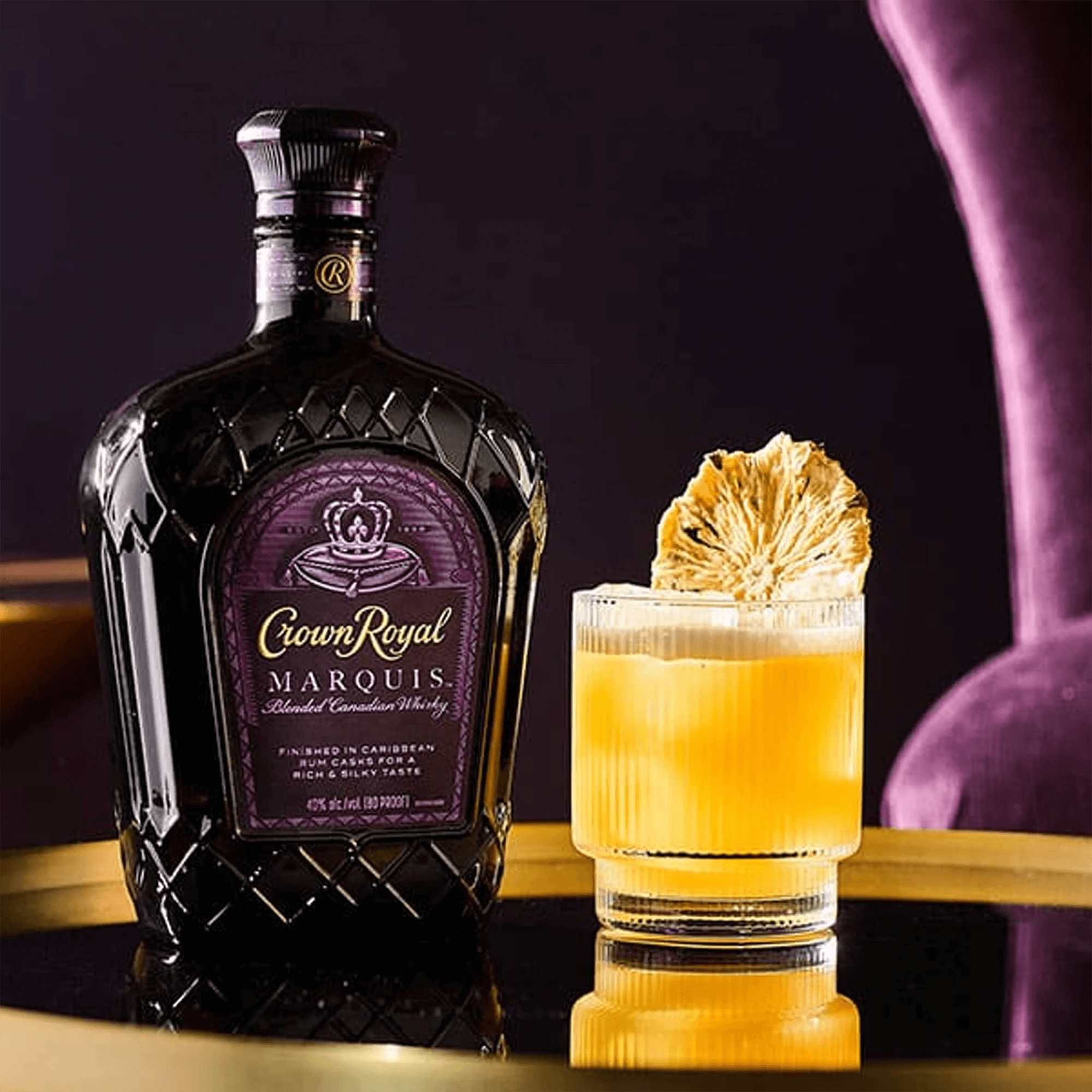 Bottle of Crown Royal Marquis whisky with a cocktail garnished with dried fruit on a stylish table.