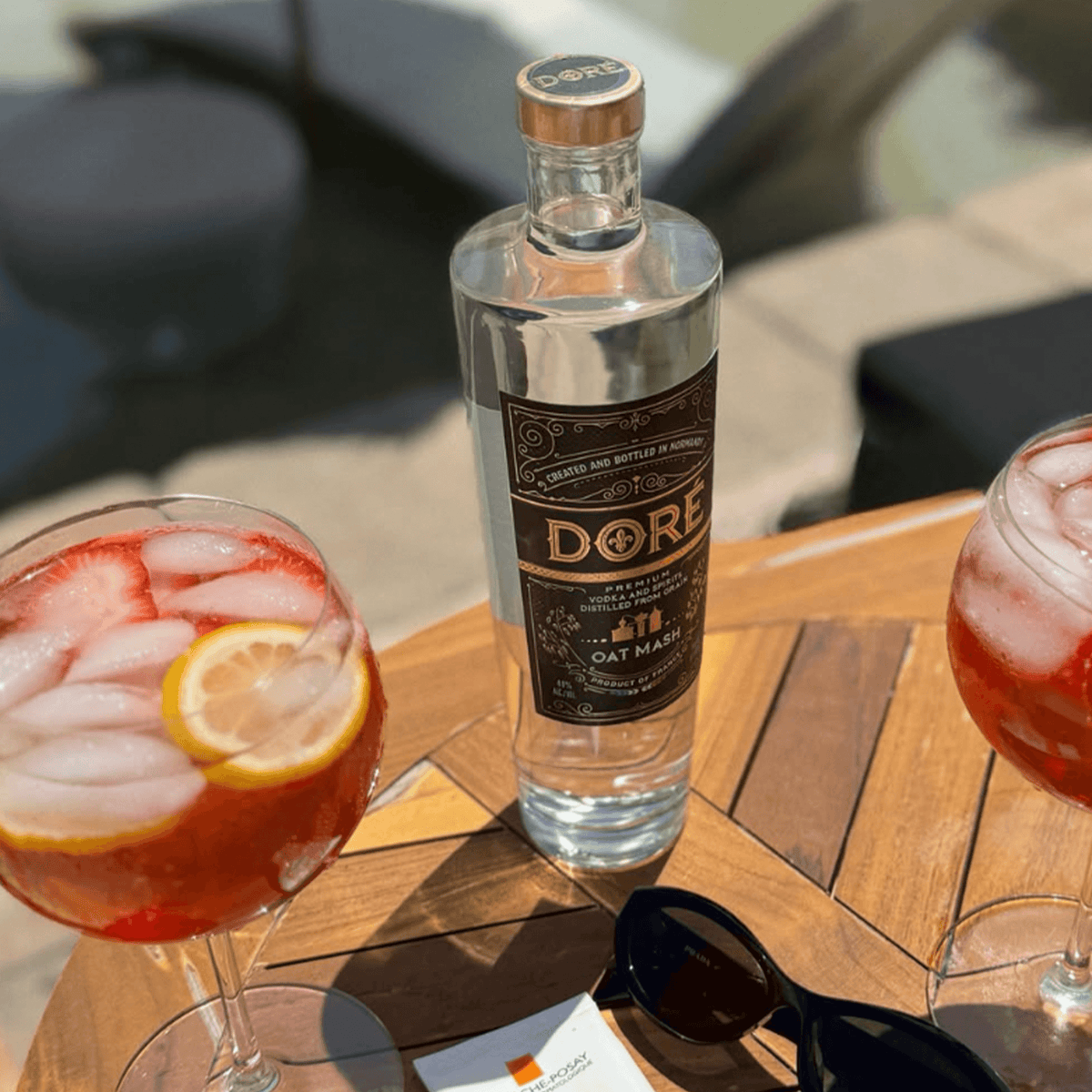 DORE Oat Mash Vodka bottle with two cocktails topped with lemon and strawberries, set on a wooden table.