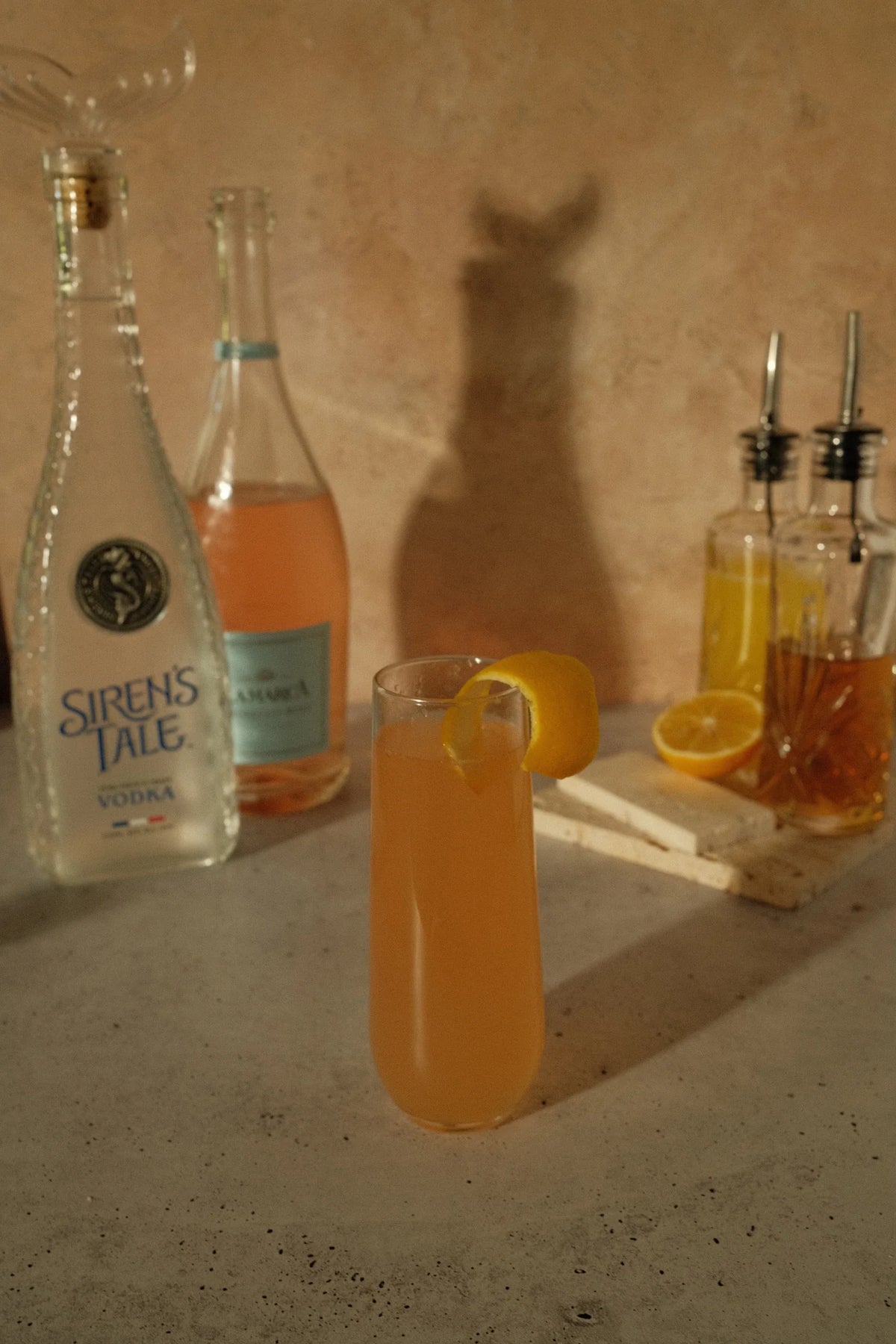 Siren's Tale French Vodka bottle with a cocktail and citrus garnishes on a textured countertop.