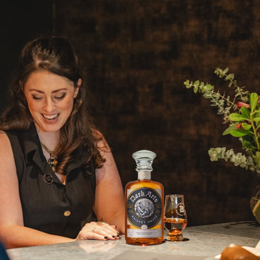 Woman enjoying Dark Arts 7 Year Cask Strength Bourbon at the bar with a glass and greenery in the background.
