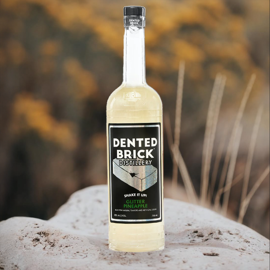 Dented Brick Glitter Pineapple rum bottle sitting on a rock with blurred autumn background.