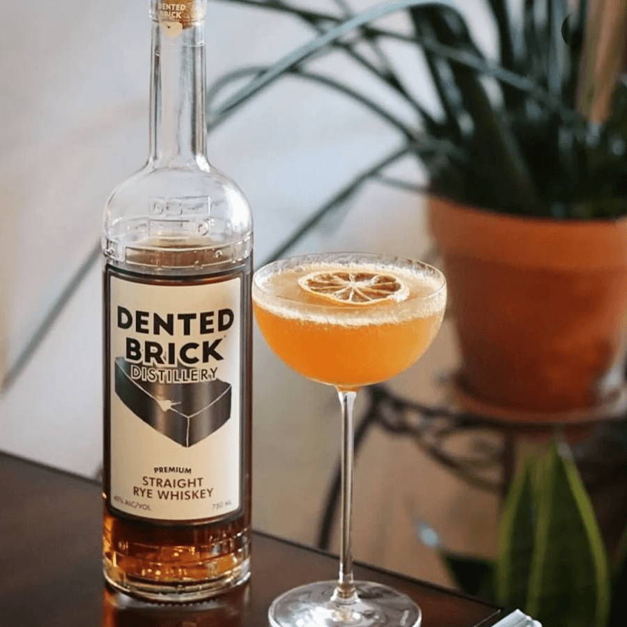 Dented Brick Premium Straight Rye Whiskey bottle next to a cocktail garnished with a lemon slice, showcasing a refined drink setting.