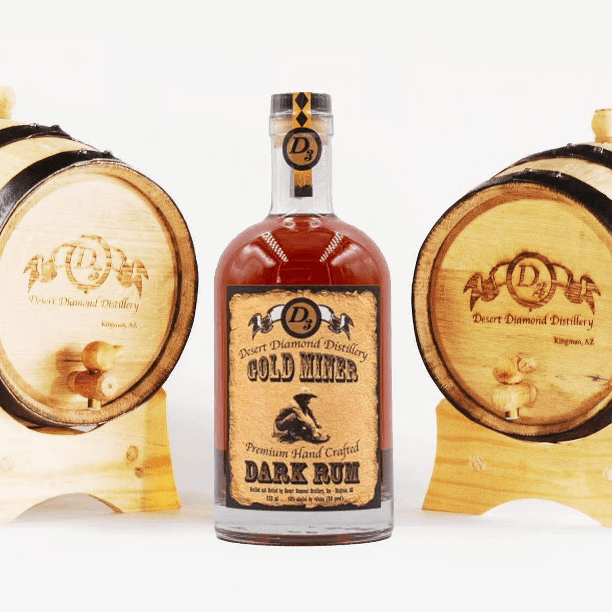 Desert Diamond Gold Miner Dark Rum bottle between two wooden oak barrels, showcasing premium handcrafted rum.