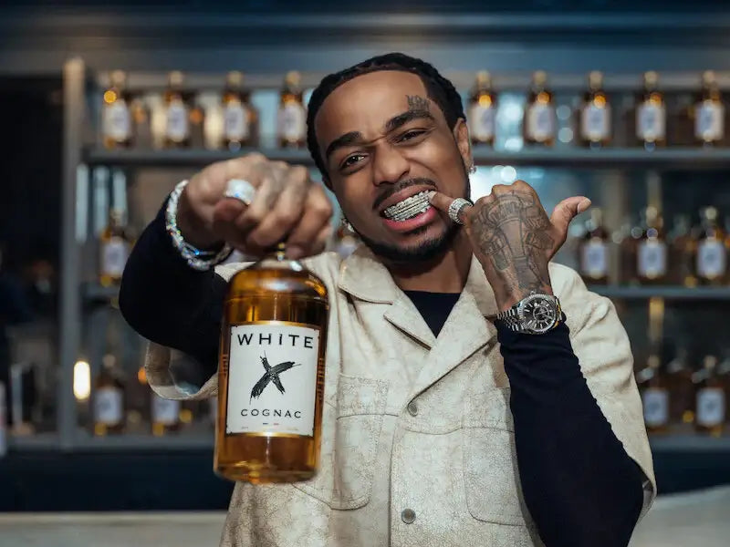 Quavo showcasing White X Cognac, a modern white cognac with 40% ABV, in a stylish setting.