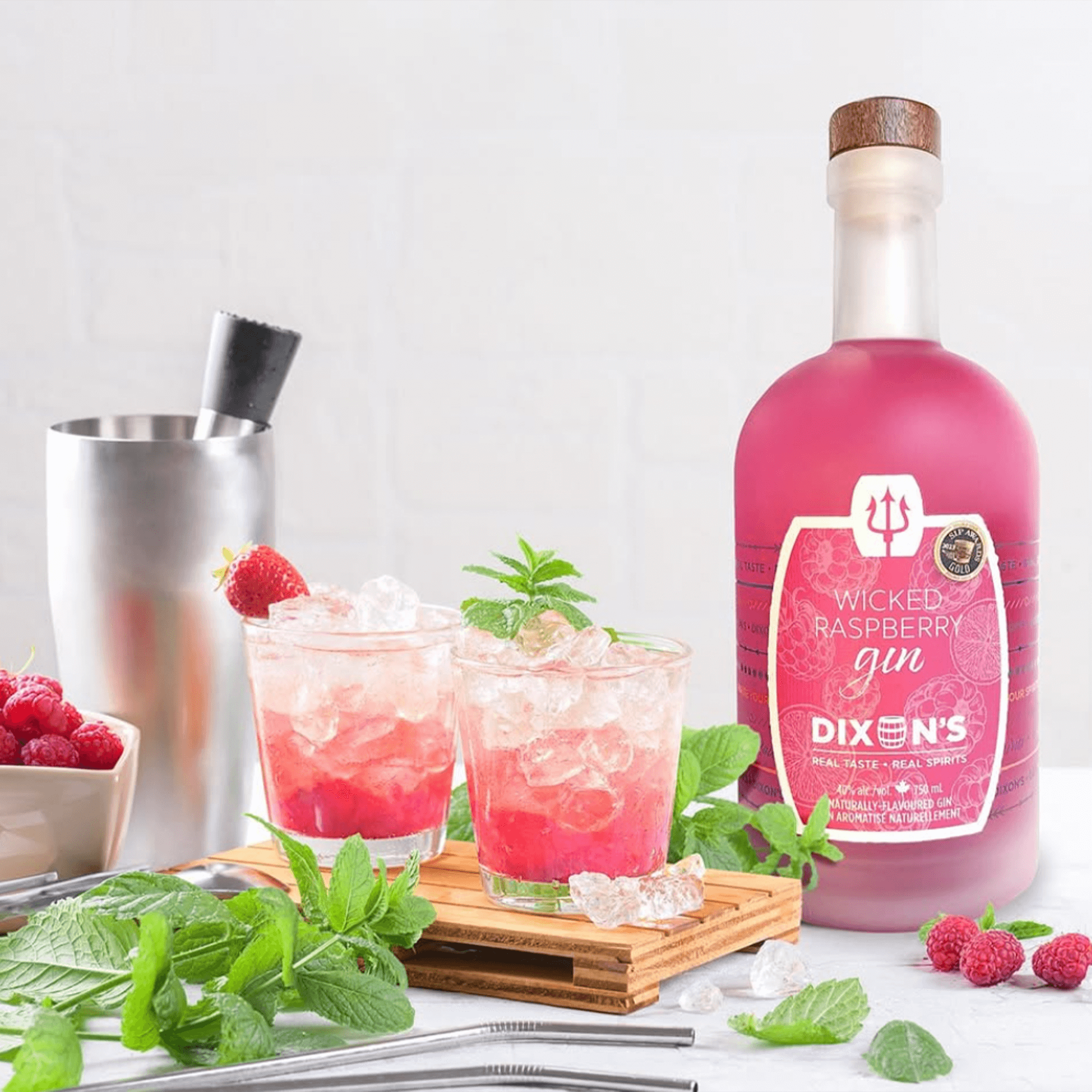 Bottles of Dixon's Wicked Raspberry Gin with cocktails and fresh raspberries on a wooden tray.