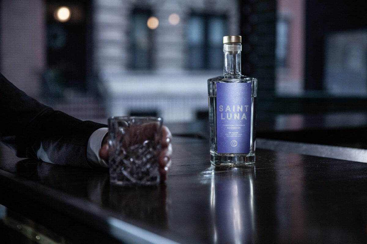 Saint Luna Charcoal Filtered Moonshine bottle on bar with a glass, showcasing its smooth and elevated taste.