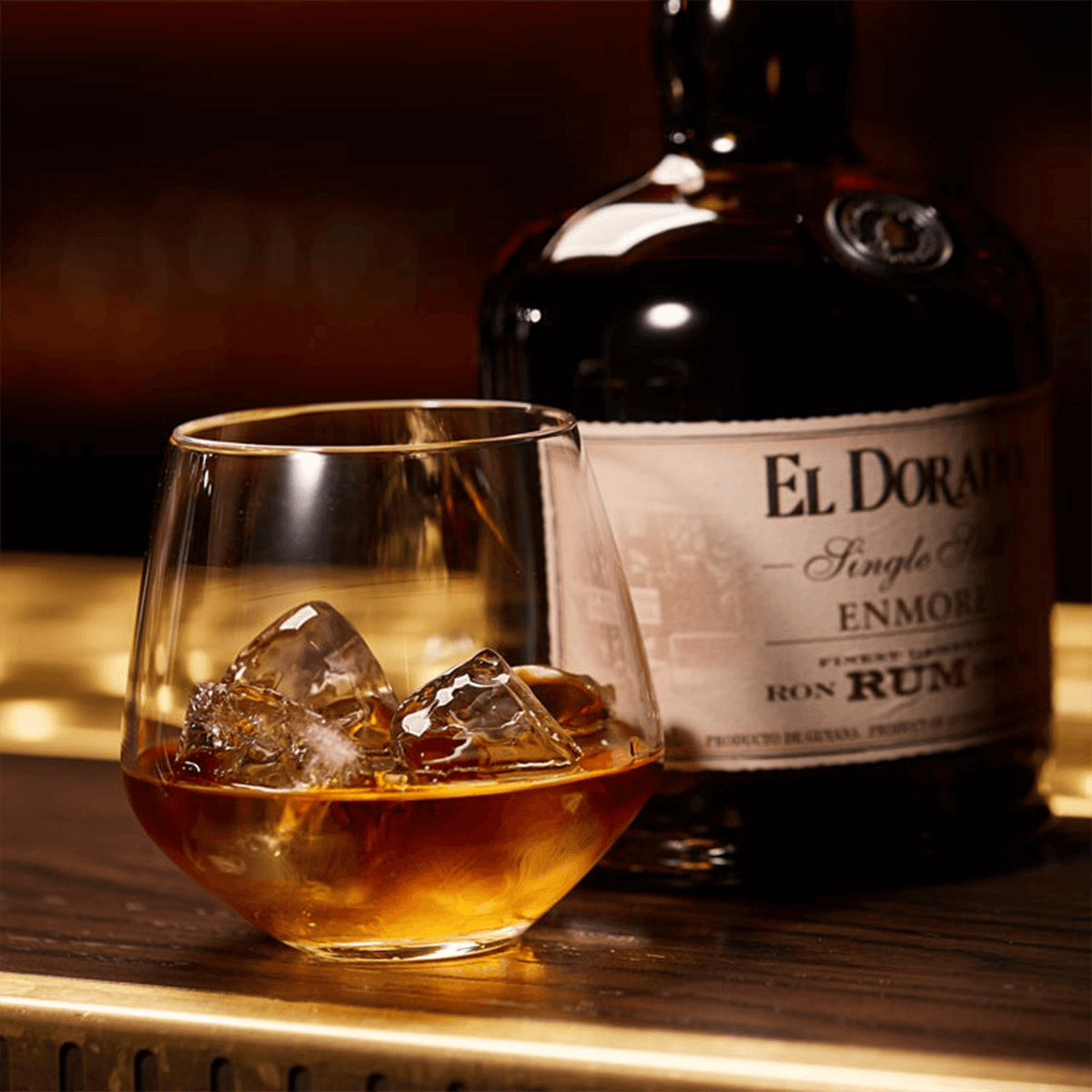 El Dorado Single Still Enmore 2009 rum in a glass with ice beside its bottle on a bar.