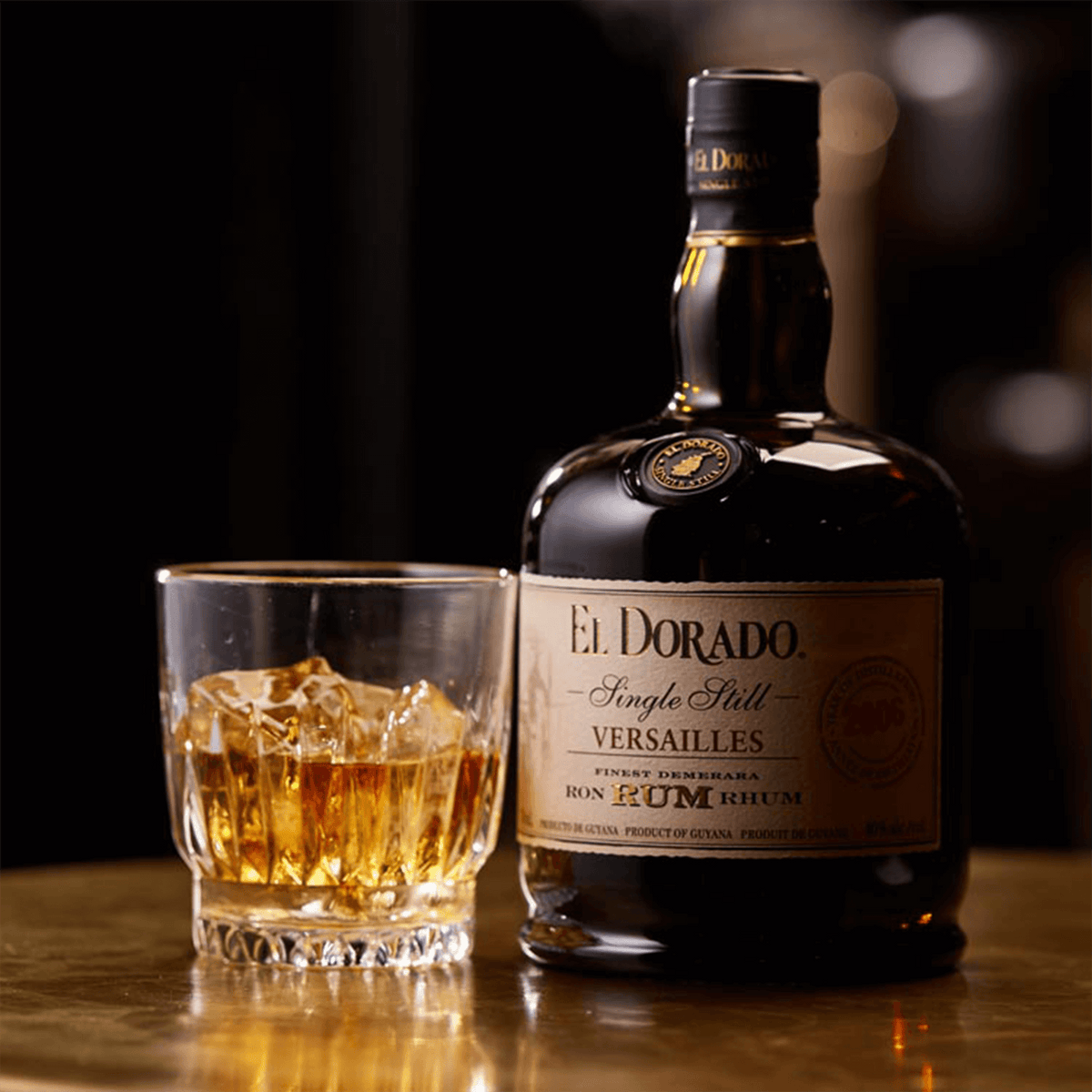 El Dorado Single Still Versailles 2009 rum bottle next to a glass of rum with ice on a wooden table.