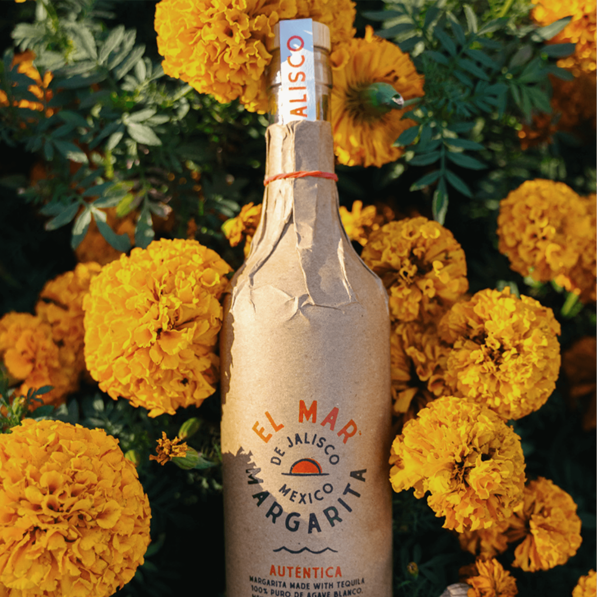 El Mar Margarita bottle surrounded by vibrant yellow marigold flowers, showcasing authentic 100% agave tequila.