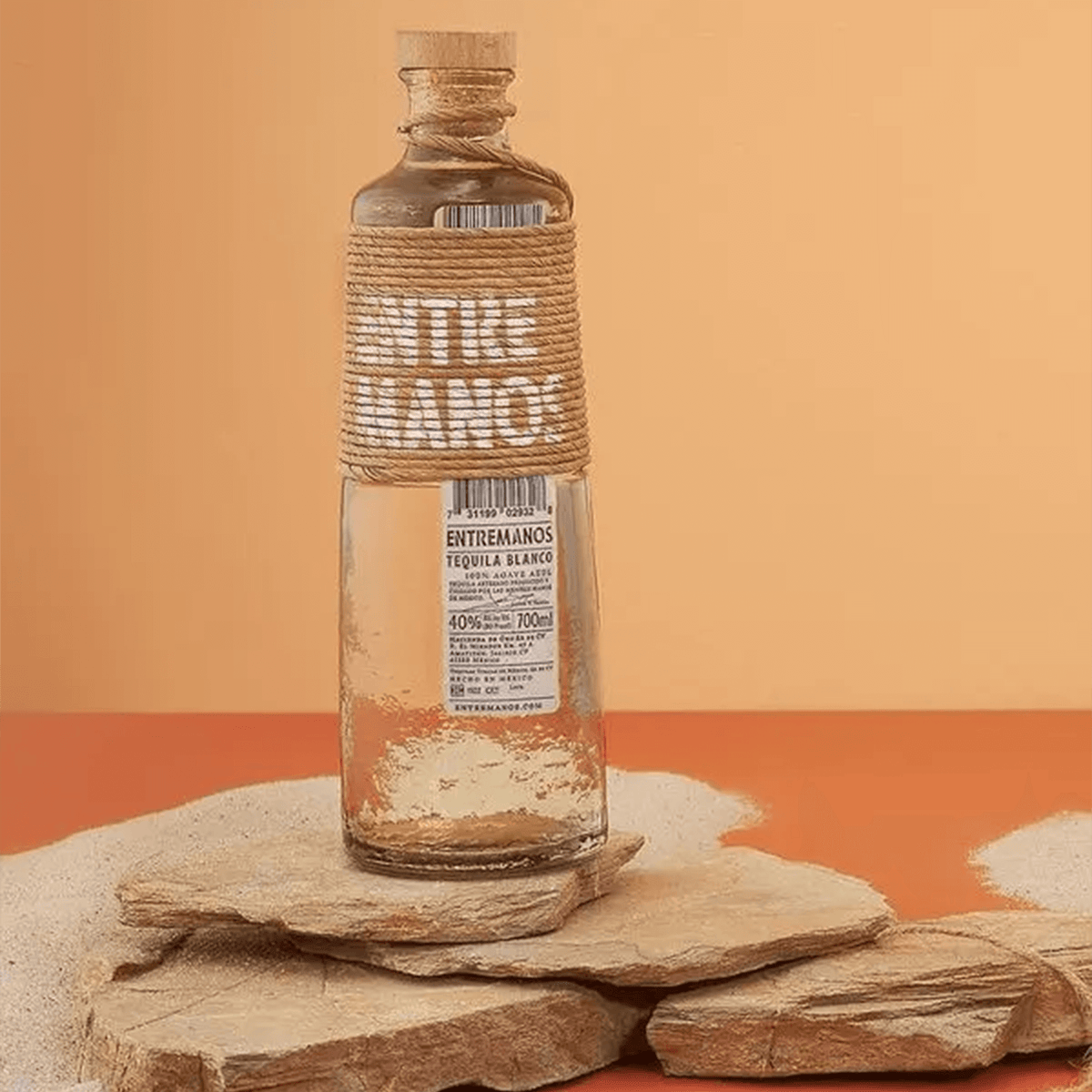Bottle of ENTREMANOS Tequila Blanco 700ml on rocks, showcasing its elegant design and 40% ABV.