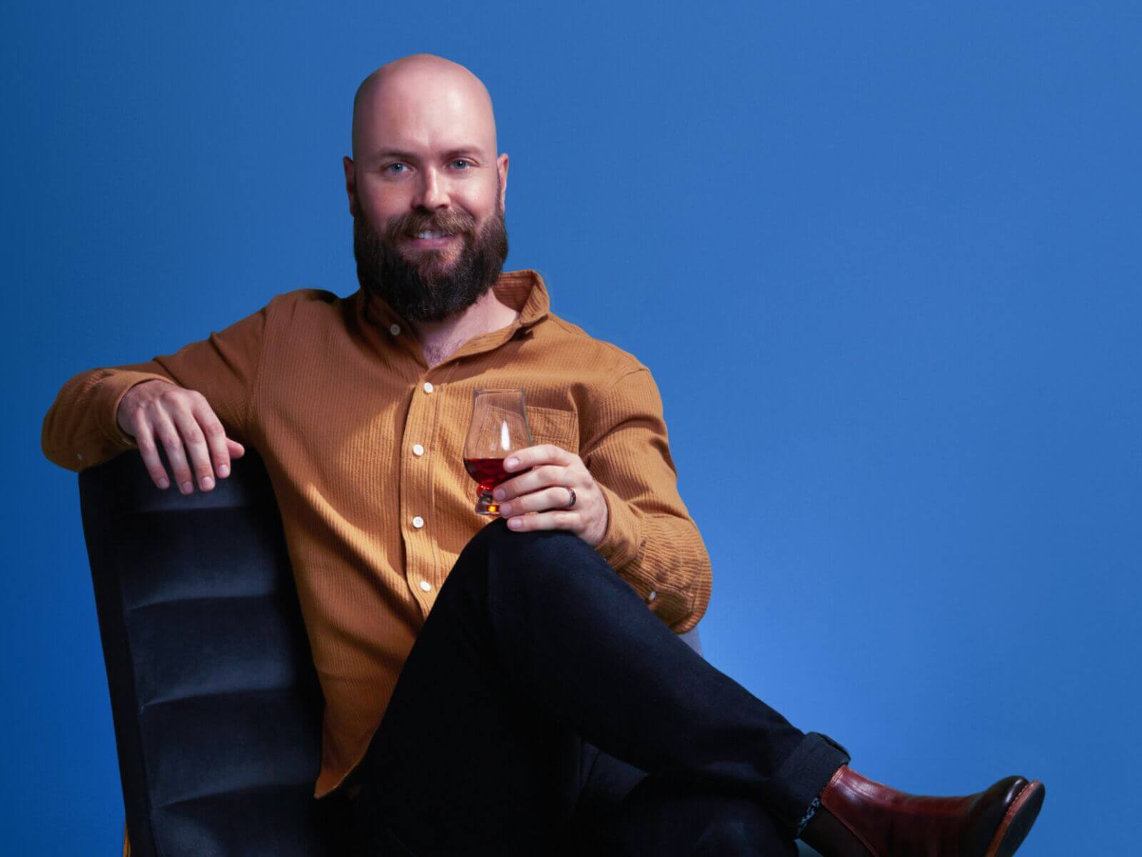 Man enjoying a glass of Angel's Envy Triple Oak Bourbon in a stylish setting with a blue background.